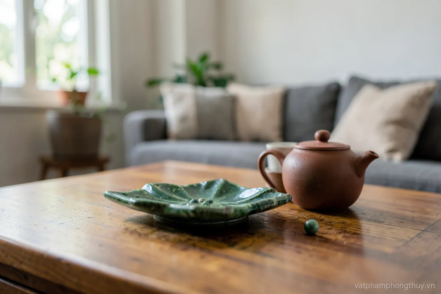 Low angle across a wooden living room tea table, a green stone seven-star dish with small spheres beside a clay teapot and cups, sofa cushions blurred behind